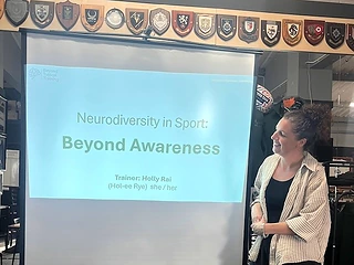 Holly Rai presenting beside a screen reading Neurodiversity in Sport: Beyond Awareness