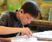 A boy wearing a hearing aid concentrating on written work at a table