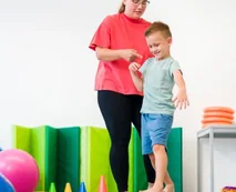 An adult supporting a young boy as he steps across soft play balance equipment