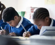 Two school pupils in blue uniforms writing at a classroom desk